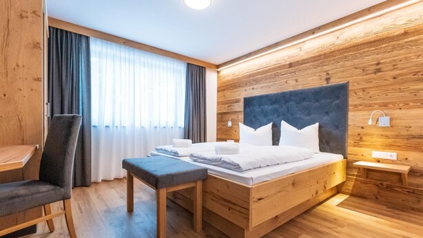 Ein Hotelzimmer mit einem hölzernen Kopfteil, einem Bett mit weißer Bettwäsche, einem Schreibtisch, einem Stuhl und einem Fenster mit Vorhängen.