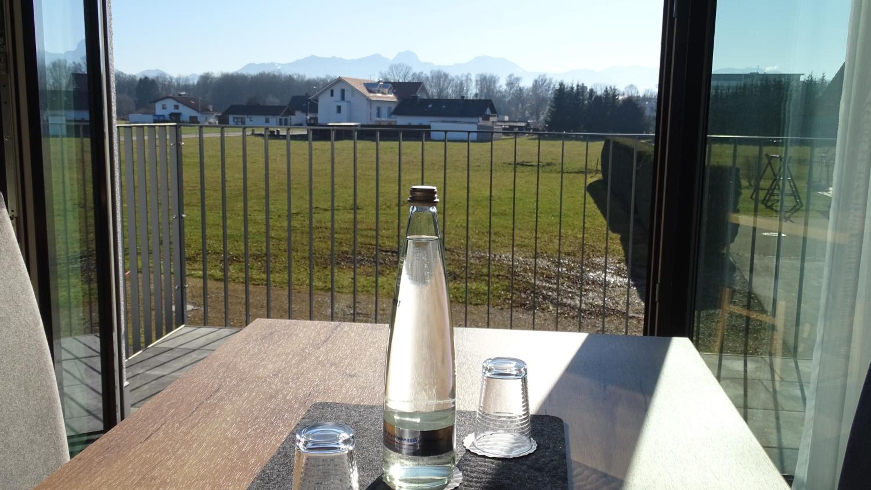 Une table avec une bouteille et des verres, donnant sur un champ verdoyant et des maisons.