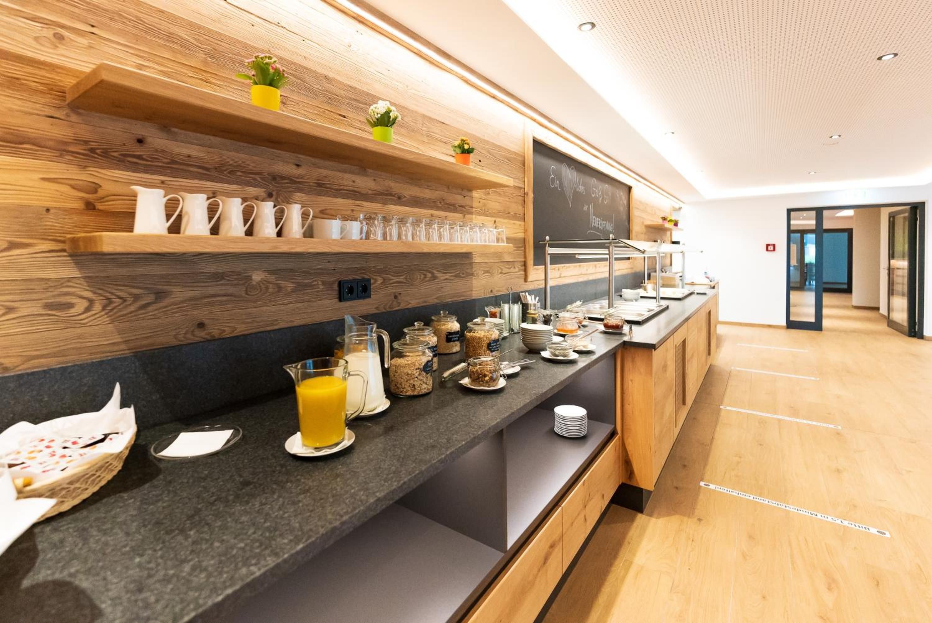 Ein Frühstücksbuffet mit verschiedenen Speisen und Getränken, Holzböden mit Tassen und eine Tafel mit Schrift.