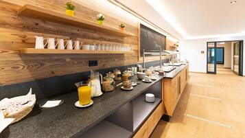 Ein Frühstücksbuffet mit verschiedenen Speisen und Getränken, Holzböden mit Tassen und eine Tafel mit Schrift.