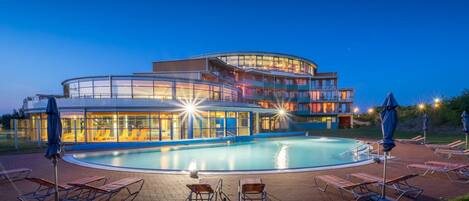 Un hotel con piscina, sillones de descanso y una terraza circular.