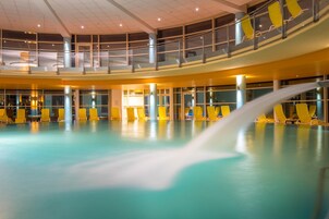 A multi-level indoor swimming pool with yellow chairs and a water feature.