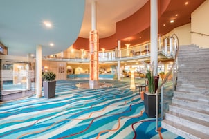A spacious lobby with a colorful carpet, a central column, and a staircase leading to an upper level.