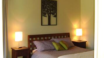 A bedroom with a sloped ceiling, a bed with a wooden headboard, two bedside lamps, and a wall-mounted picture of a tree.