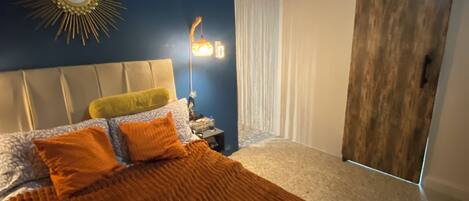 A bedroom with a bed, a nightstand, a wall-mounted mirror, a hanging light fixture, and a sliding door.