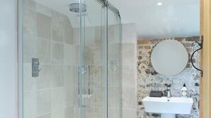 A modern bathroom with a glass-enclosed shower, a white sink, and a stone-patterned wall. - Shepherds Barn (Chichester)