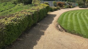 A gravel path leading to a green lawn with a fence and trees in the background. - Shepherds Barn (Chichester)