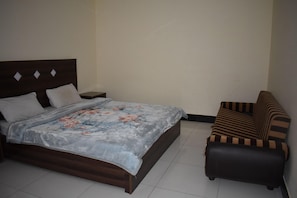 A bedroom with a bed, a nightstand, a sofa, and a plain wall. - Hotel 1947 (Balakot)