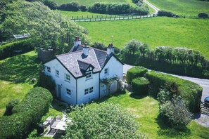 A large white house with a steep roof, surrounded by lush green fields and a fenced area. - Dollars Cottage 4 Bed Llangennith (Swansea)