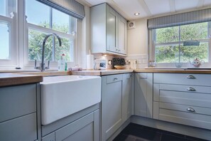 A modern kitchen with a built-in dishwasher, a sink with a faucet, and a window with a view of greenery. - Dollars Cottage 4 Bed Llangennith (Swansea)