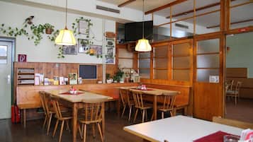 Interior de restaurante con mesas y sillas de madera, lámparas colgantes y una pared decorada con marcos de fotos y plantas.