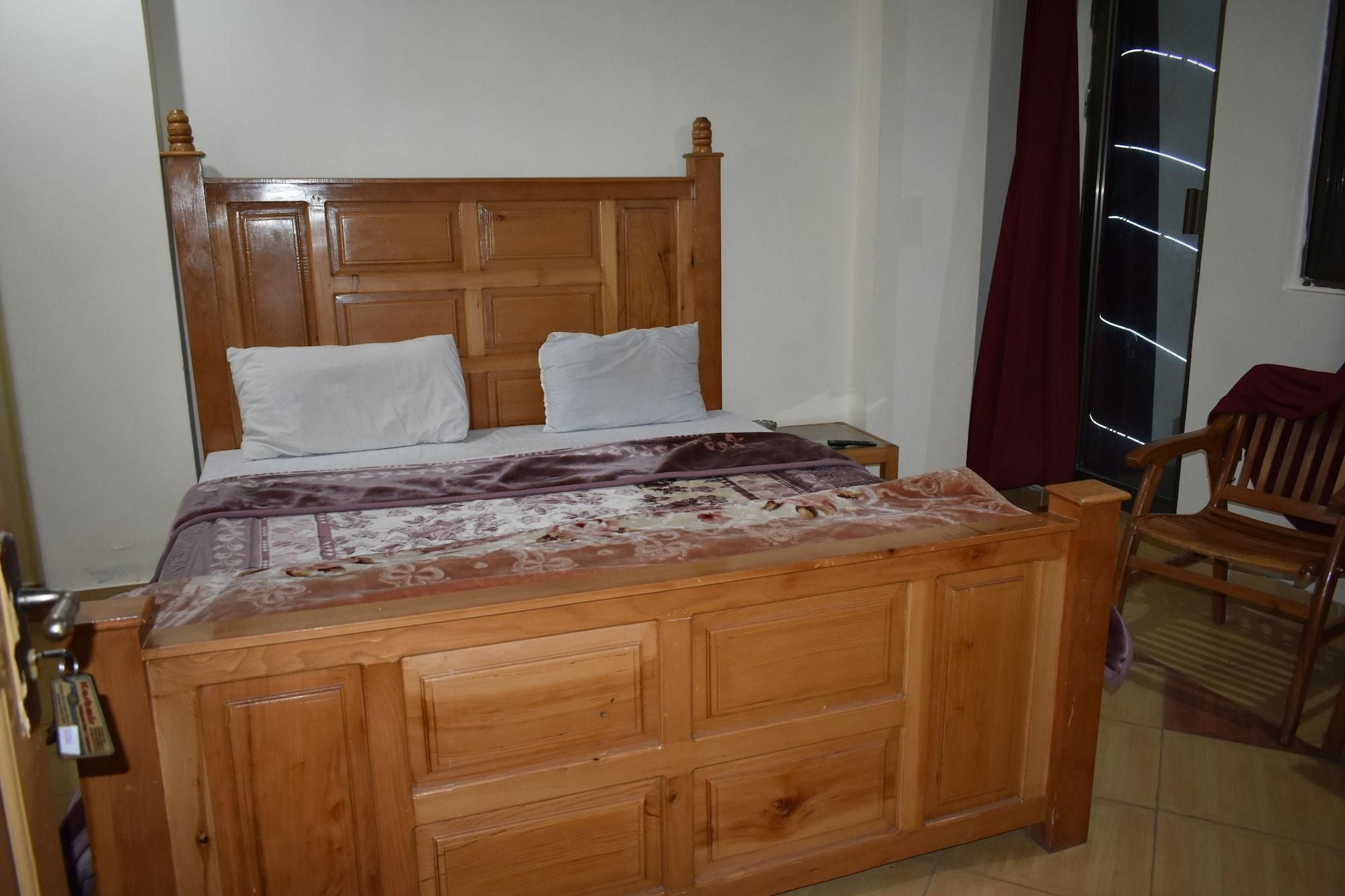 Una cama de madera con cabecera, dos almohadas y una colcha estampada.