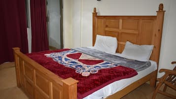 Una cama de madera con colcha de diseño rojo y blanco, un almohadón blanco y un cabecero de madera.