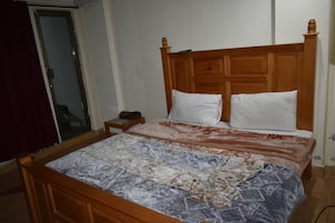 Un dormitorio con cabecera de cama de madera, dos almohadas, una mesita de noche y una colcha estampada.