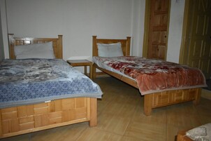 Dos camas de madera con cabeceras, una mesita de madera y una puerta de madera en una habitación con piso de baldosas.
