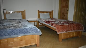Dos camas de madera con cabeceras, una mesita de madera y una puerta de madera en una habitación con piso de baldosas.