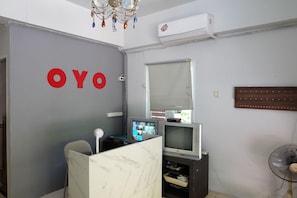 A room with a grey wall, a white air conditioning unit, a television, a fan, and a decorative chandelier. - Pop 75429 101 Place Navanakorn (Bangkok)