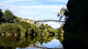 A river with a bridge, surrounded by trees and a building in the background.