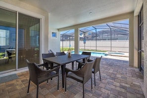 An outdoor patio with a table and chairs, a glass door, and a view of a swimming pool. - Ultimate Resort Retreat, Stunning 6-bedroom Haven (Kissimmee)