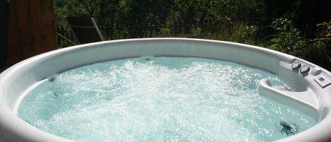 Un jacuzzi al aire libre con una estructura de madera a la izquierda y un área boscosa al fondo.