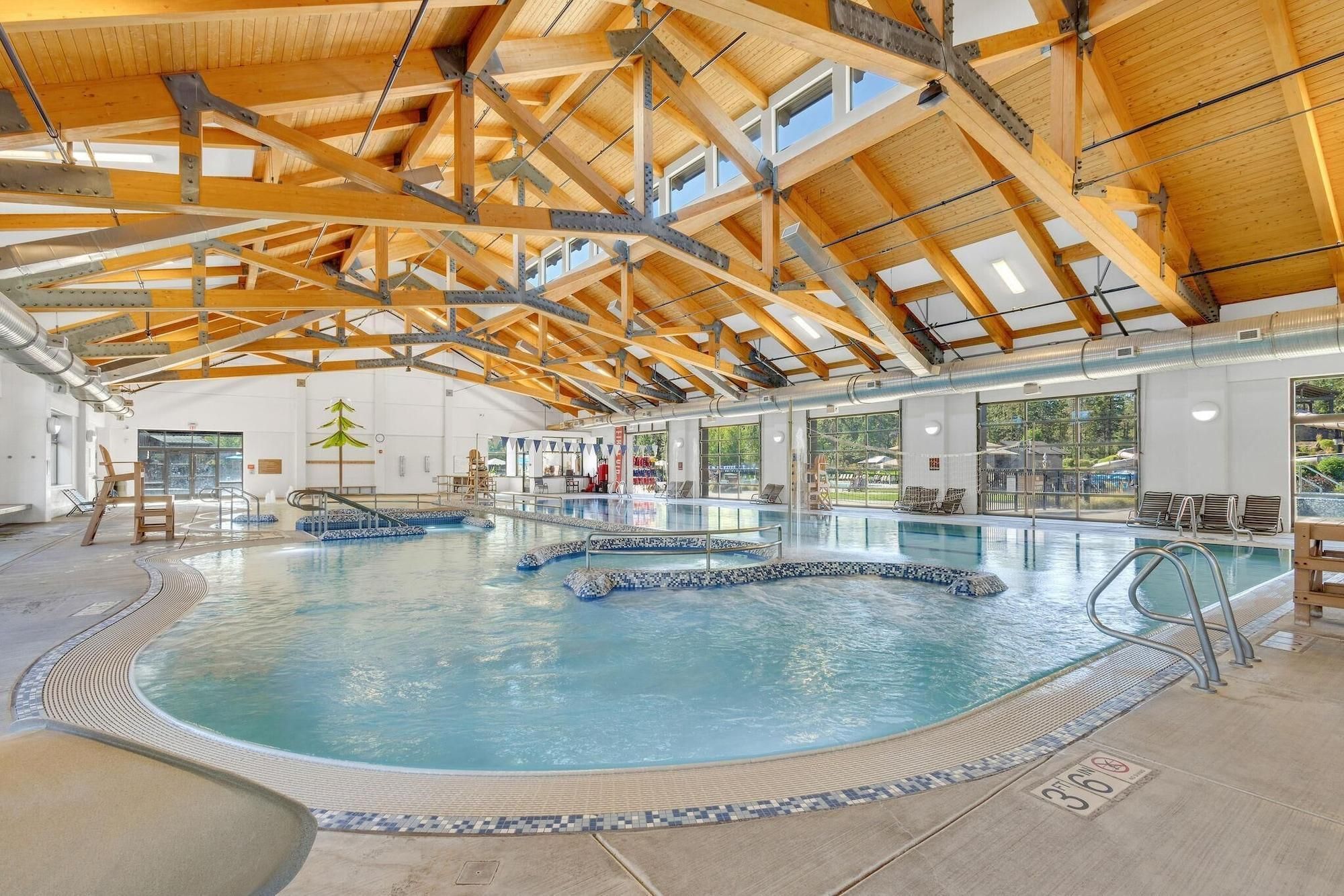 An indoor swimming pool with multiple lanes, a wooden ceiling structure, and a view of the outdoors through large windows.