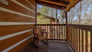 A wooden deck with a bench, a wooden railing, and a view of a cabin in the background. - Cozy Bears Cabin (Pigeon Forge)
