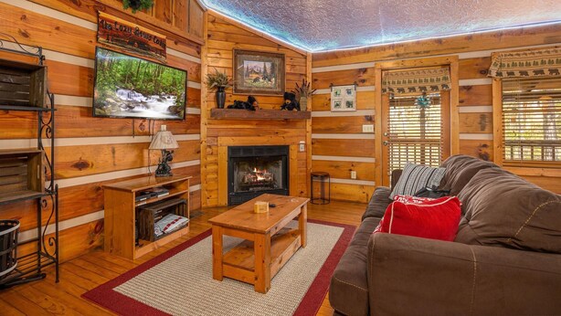 A log cabin interior with a fireplace, wooden walls, a television, and a sofa. - Cozy Bears Cabin (Pigeon Forge)