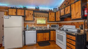 A compact kitchen with wooden cabinets, a refrigerator, a microwave, an oven, and a sink. - Cozy Bears Cabin (Pigeon Forge)