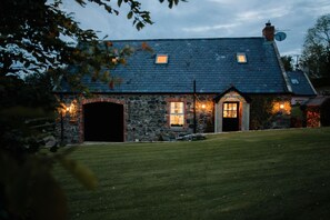 Uma casa de pedra com telhado escuro, duas janelas e um gramado bem cuidado.