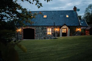 Uma casa de pedra com telhado escuro, duas janelas e um gramado bem cuidado.