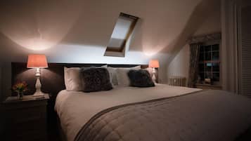 A bedroom with a large bed, two bedside lamps, a nightstand, and a window with curtains.