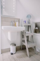 Casa de banho com lavatório branco, espelho e prateleira com artigos de higiene pessoal.