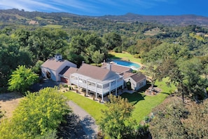 A large house with a pool, surrounded by lush greenery and hills.
