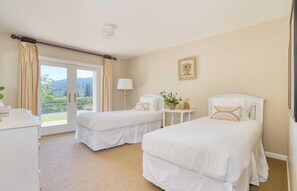 Habitación de hotel con dos camas, una ventana con cortinas, una mesita de noche con lámpara y un cuadro enmarcado en la pared.