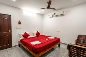 Un dormitorio con cama, ventilador de techo, unidad de aire acondicionado, puerta de madera y una silla.