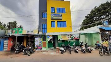 A multi-story building with a yellow facade, several ground-level shops, and parked scooters.