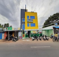 Un edificio de varios pisos con fachada amarilla y varias tiendas en la planta baja, además de scooters estacionados.