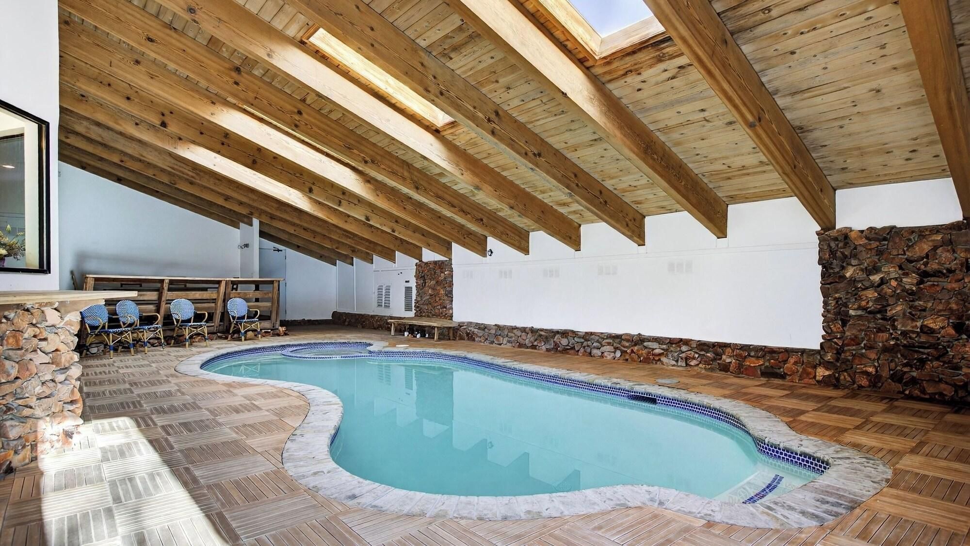 Piscina interna com parede de pedra e piso de deck de madeira.