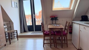 A small kitchenette with a window, a dining table with chairs, and a view of buildings outside. - Hotel Cafe De Harmonie (Edam)