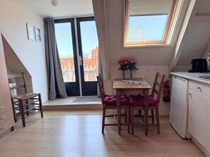 Uma pequena cozinha compacta com janela, uma mesa de jantar com cadeiras e vista para edifícios.