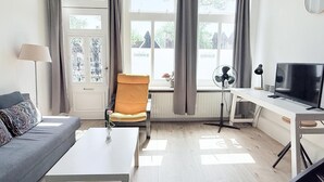 A modern living room with a sofa, a chair, a coffee table, a TV, and a radiator. - Hotel Cafe De Harmonie (Edam)