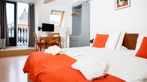 A hotel room with a large bed, a desk with a computer, and a view of a building outside. - Hotel Cafe De Harmonie (Edam)