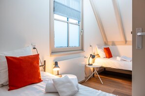 Un dormitorio con techo inclinado, una ventana con vistas, dos mesitas de noche con lámparas y una cama con almohadas.