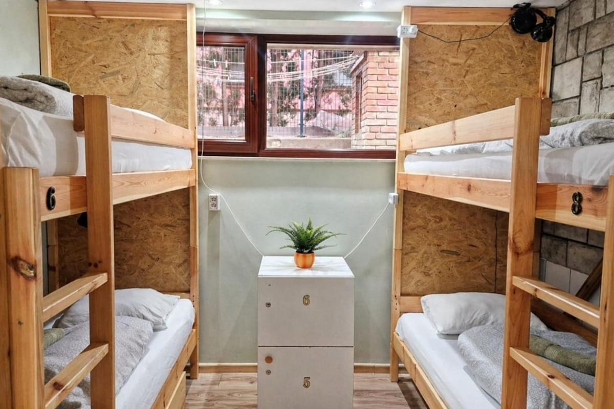 A dormitory room with bunk beds, a small cabinet, and a window.