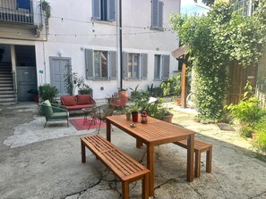 Um pátio com mesa e bancos de madeira, rodeado por plantas em vasos e um sofá vermelho.