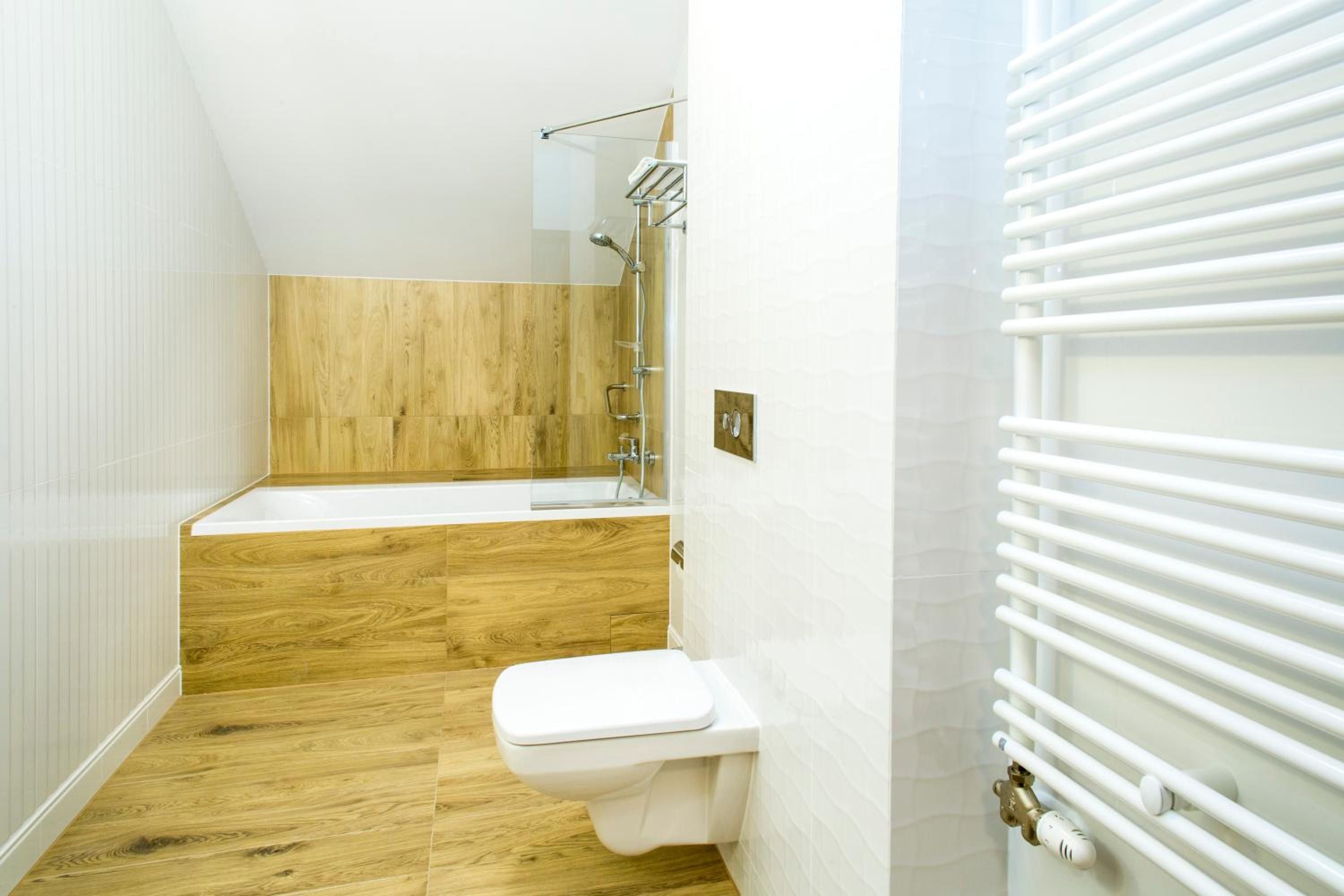 A bathroom with a wooden floor, a white toilet, a bathtub, and a shower with a glass enclosure.