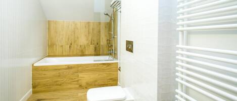 A bathroom with a wooden floor, a white toilet, a bathtub, and a shower with a glass enclosure.