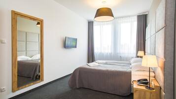 Ein Hotelzimmer mit einem Bett, einem Nachttisch mit Lampe, einem Spiegel und einem Fenster mit Vorhängen.
