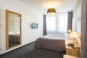 Habitación de hotel con cama, mesita de noche con lámpara, espejo y ventana con cortinas.