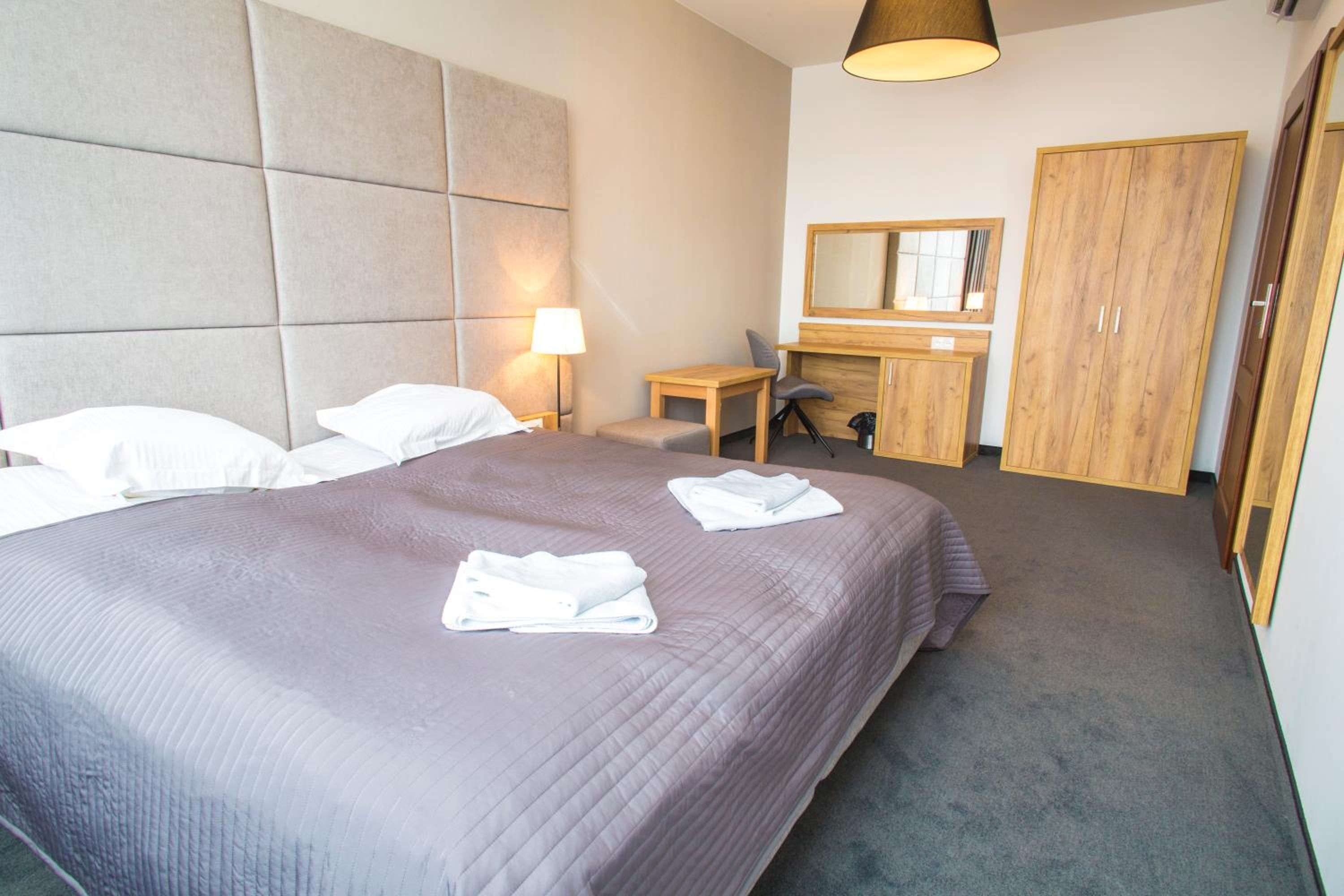 Quarto de hotel com uma cama grande, uma escrivaninha, um espelho e um guarda-roupa.